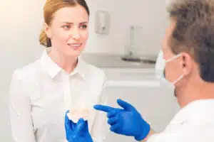 An orthodontist holding a dental model while talking to a female patient.