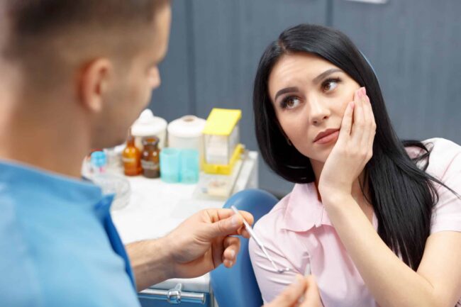 Patient with Toothache Consulting Dentist A female patient holding her painful jaw while talking to her dentist.