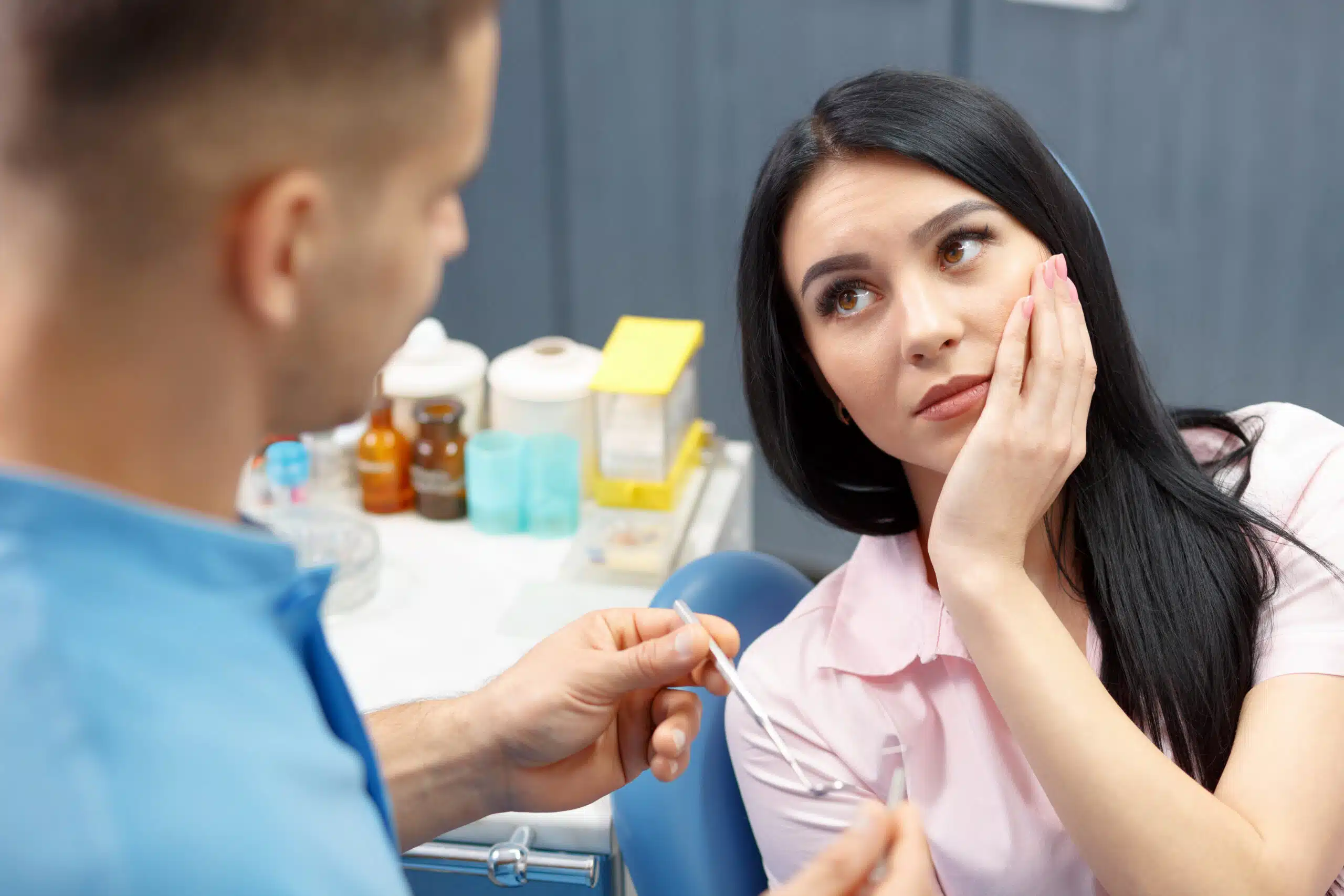 A female patient holding her painful jaw while talking to her dentist.